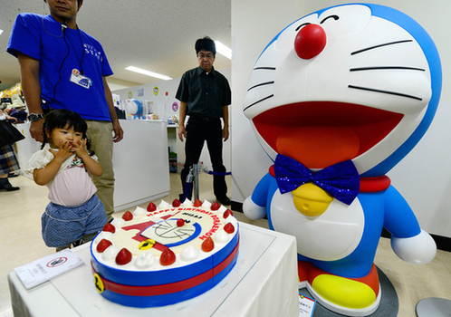 2013年9月3日，在日本东京举行的一个展览上，一名小朋友欣赏哆啦A梦玩偶以及它的生日蛋糕。图片：新华社/法新